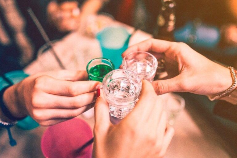 três pessoas brindando com cachaça em um bar