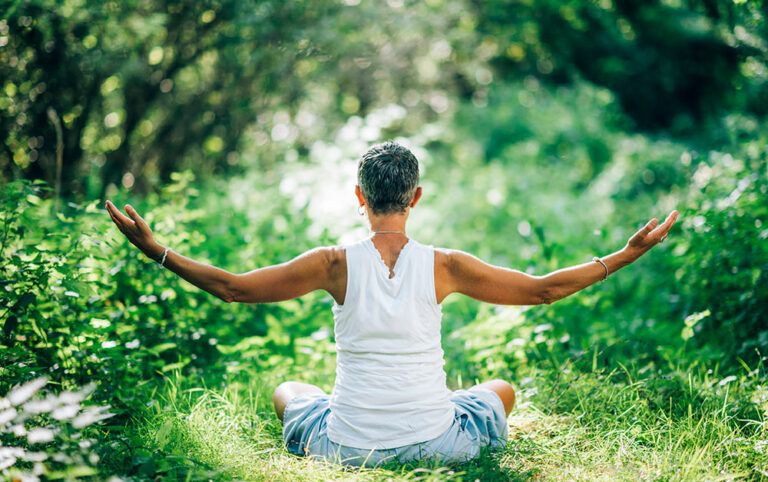 Uma mulher sentada em meio a natureza desfrutando dos benefícios do turismo terapêutico