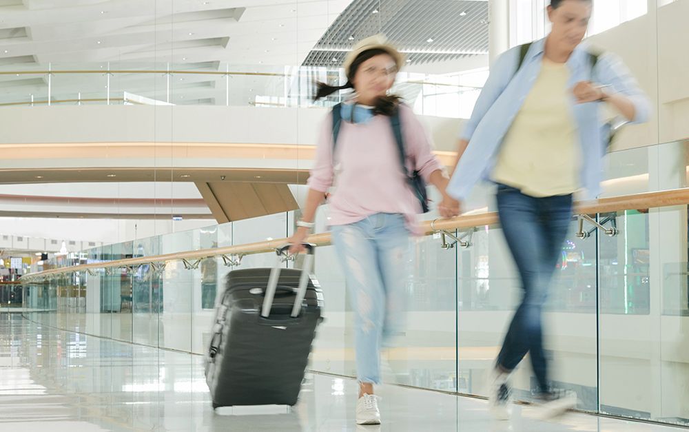 Um homem e uma mulher correndo de mãos dadas com uma mala de rodinhas para não perder a viagem de última hora