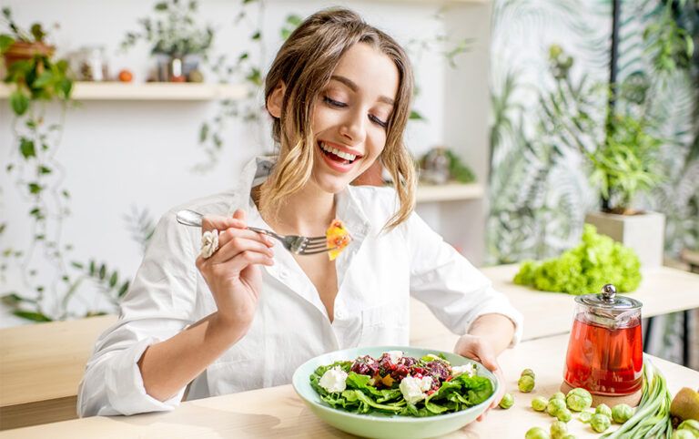 Mulher sentada à mesa em uma cozinha, comendo salada, um dos lanches leves citados no texto